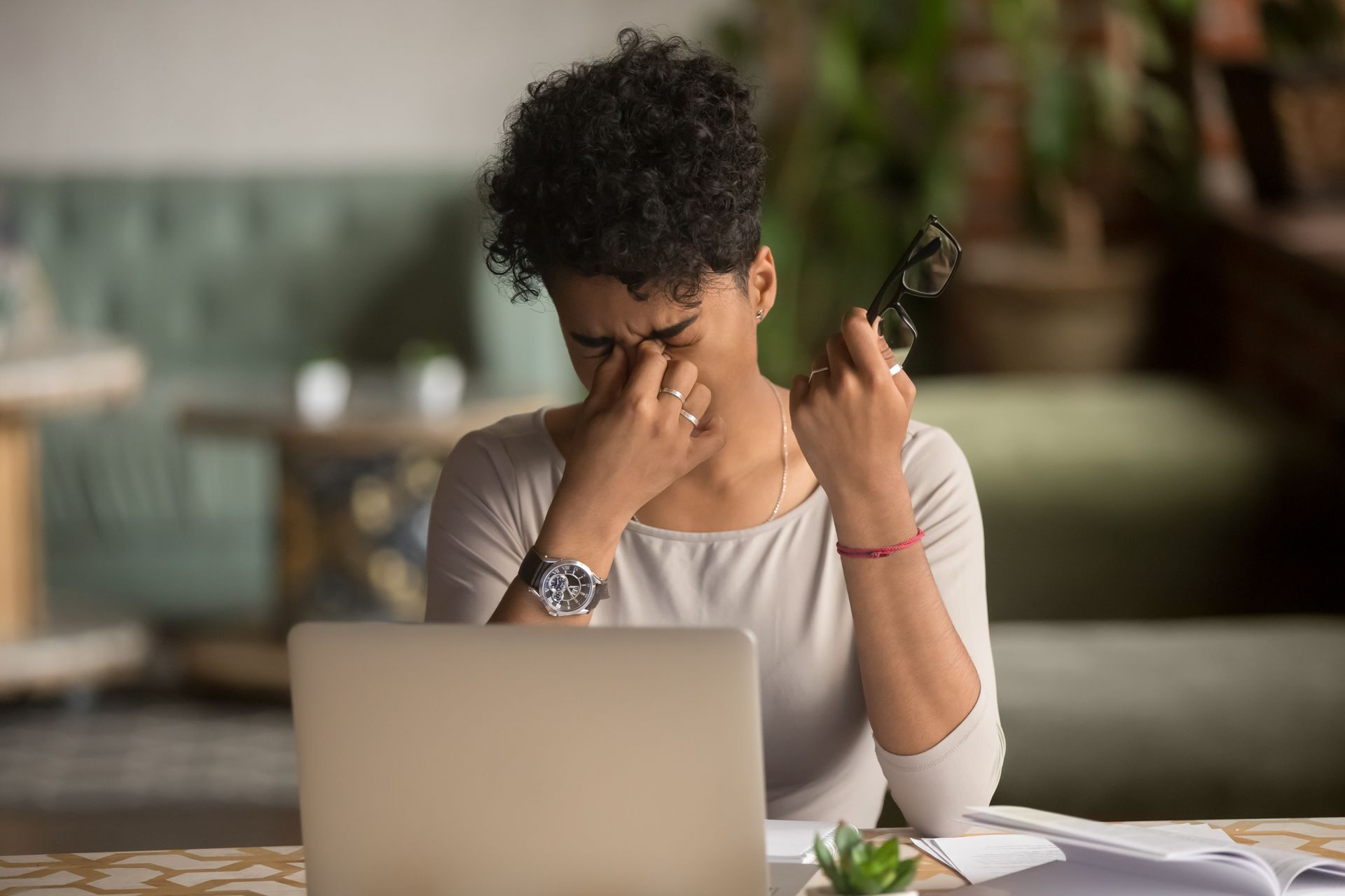 a woman sits in a coffee shop, pinching the bridge of her nose, she is feeling emotionally overwhelmed