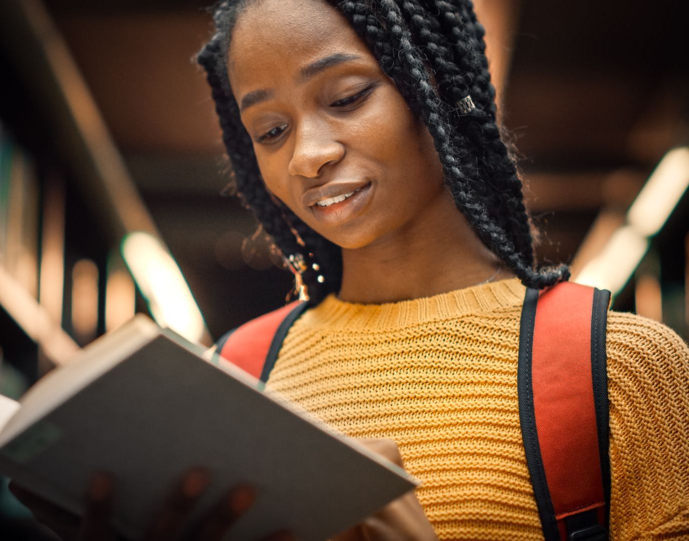 The young college student reads a book in an asile of the library, she is working on her steps for goal setting