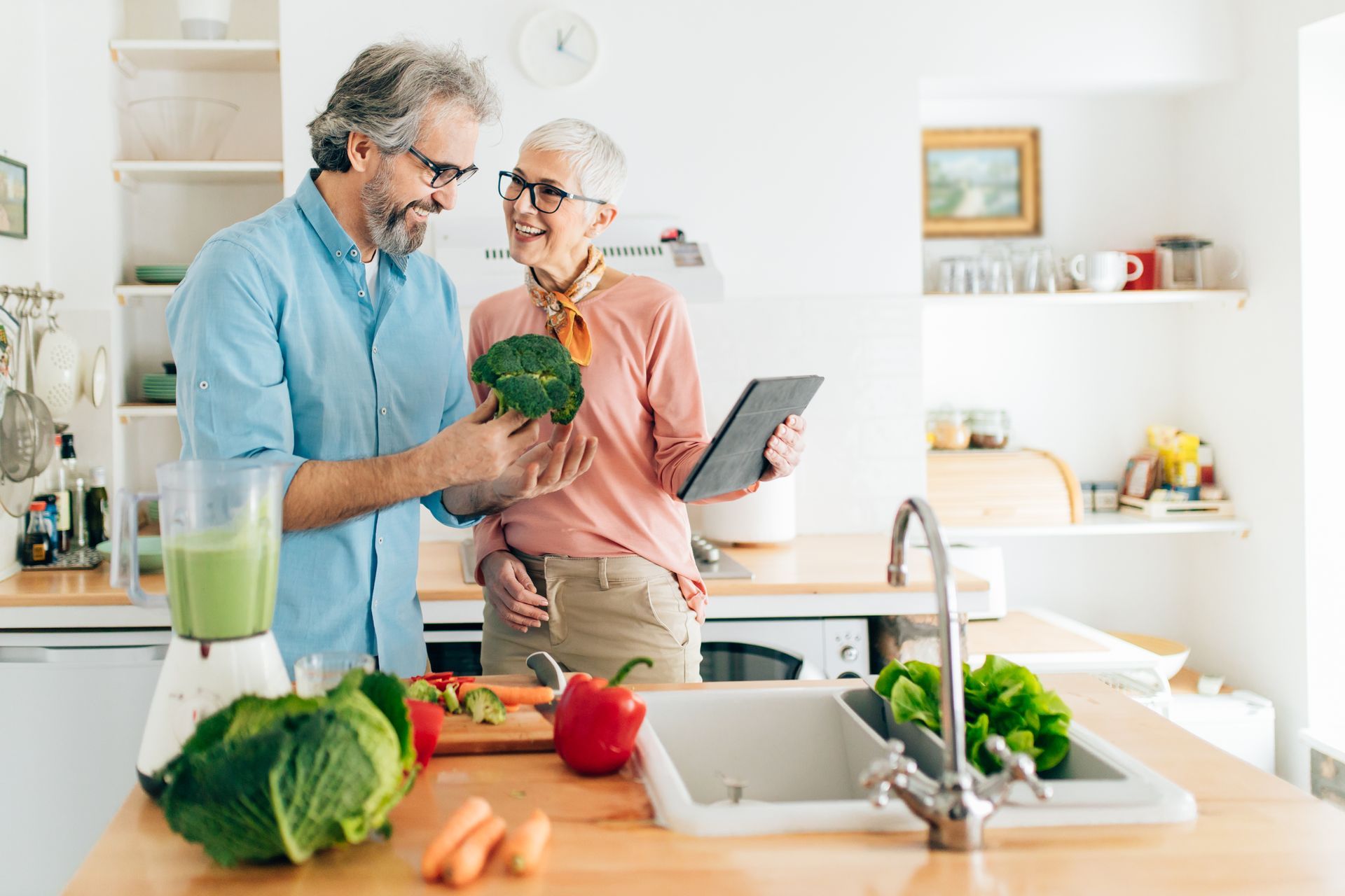 a man is holding a broccoli and a woman is holding a tablet in a kitchen, embodying the 5 stepping stones in a relationship