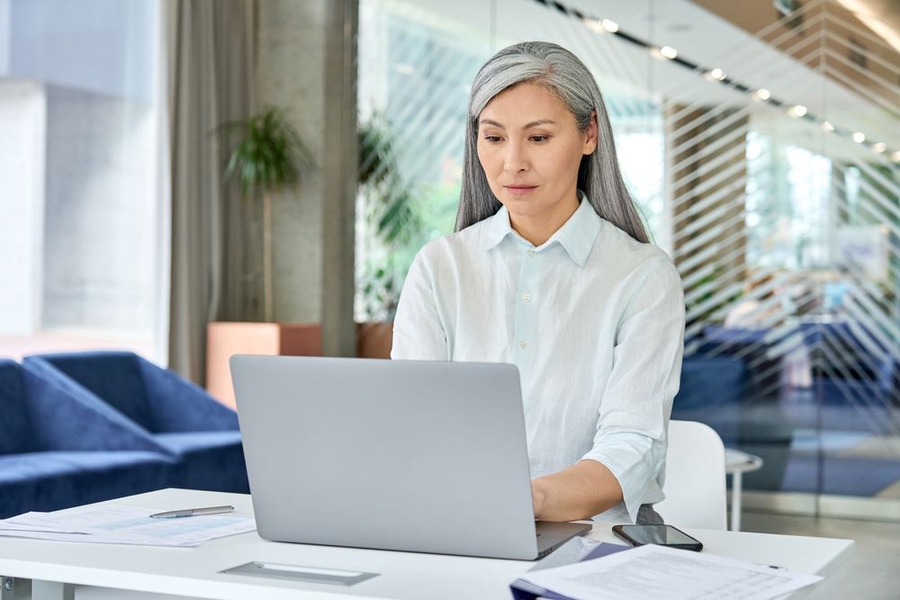 a woman is sitting at a desk using a laptop computer, reflecting on her personal pride