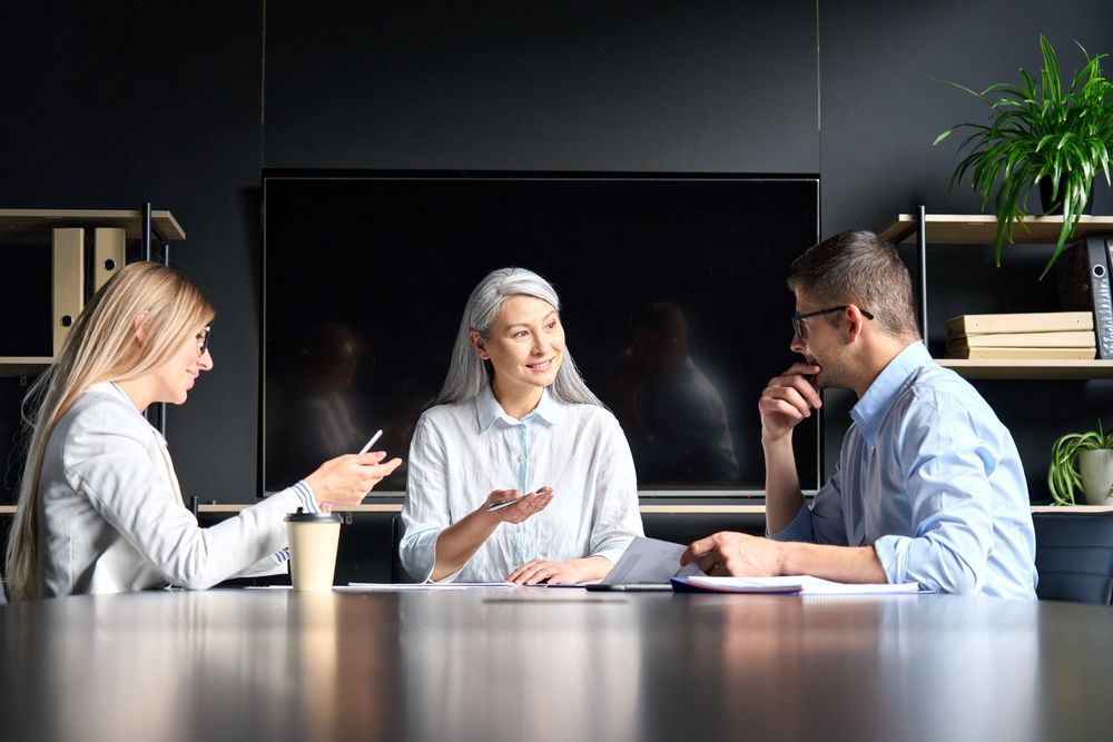 the woman and two additional people are sitting at a table having a meeting, facing the consequences of her pride and overcoming it