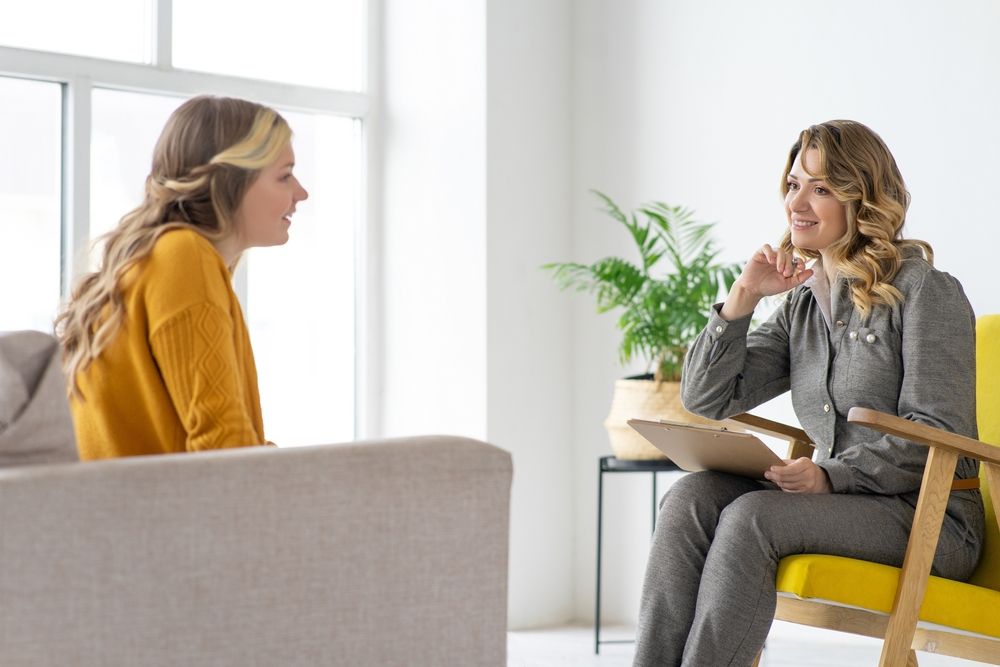 A woman is sitting in a chair talking to another woman.