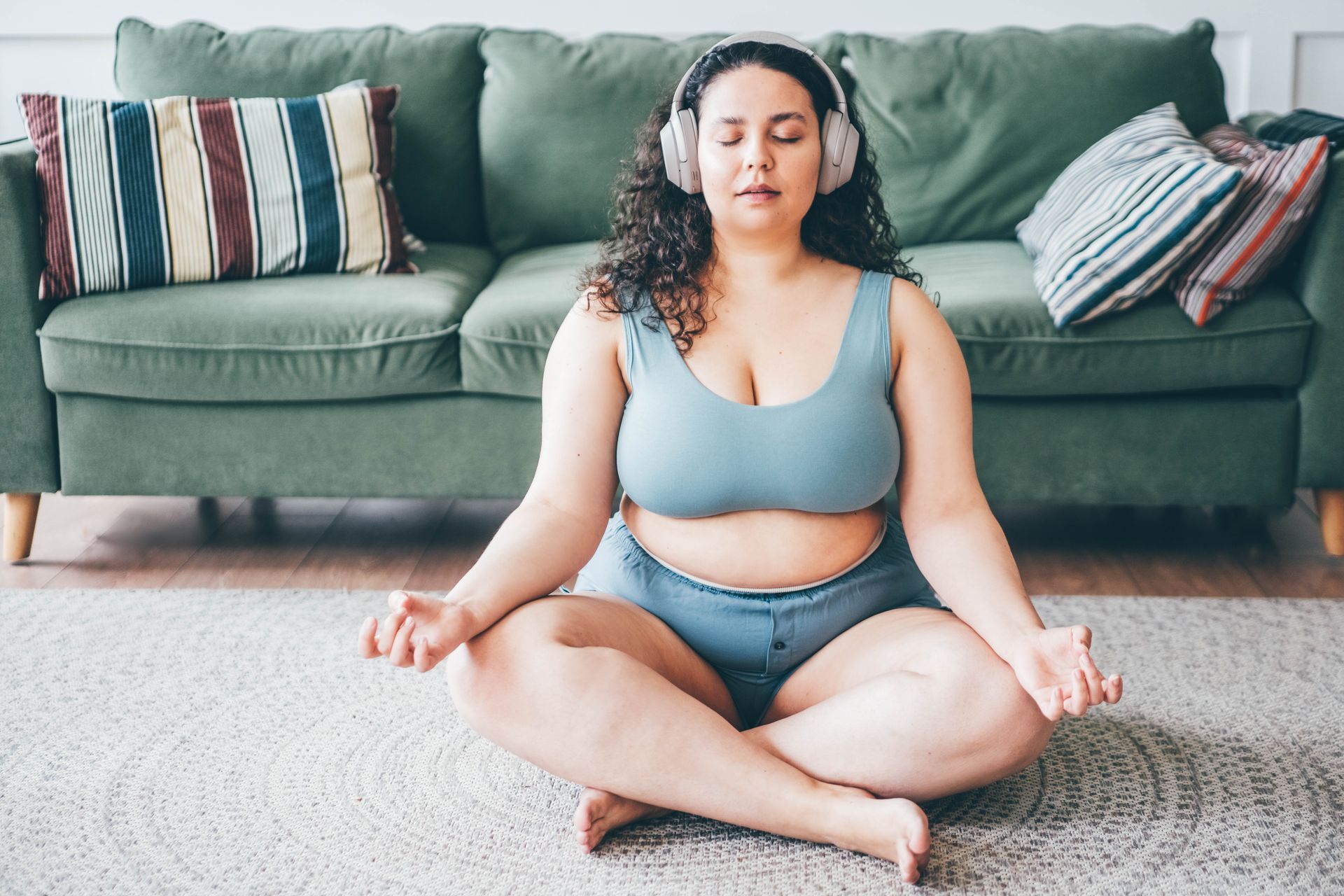 A woman sits on the floor meditating with headphones on, she is contemplating motivation vs discipline