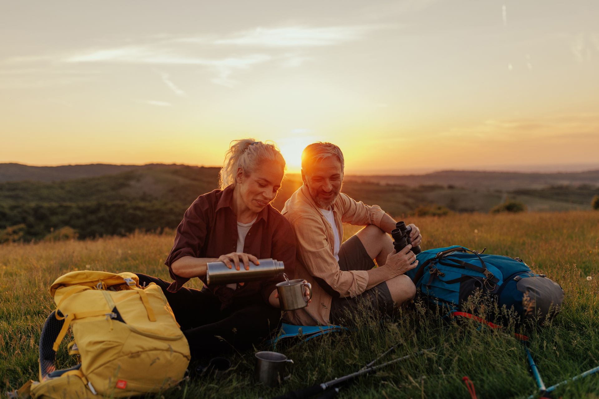 A man and a woman are sitting in a field at sunset contemplating perseverance vs persistence after their hike