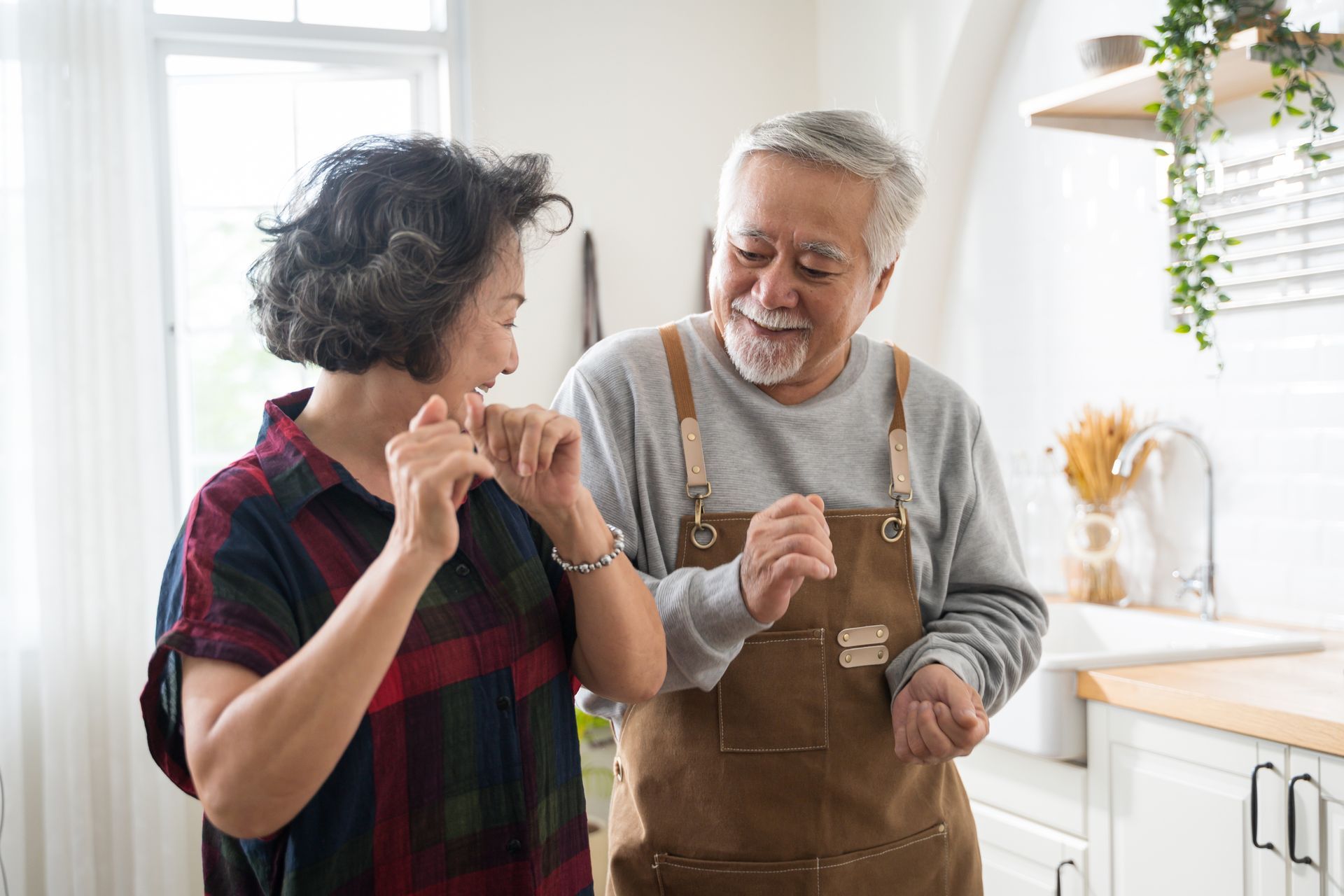 an elderly Asian couple dance together in their kitchen while cooking,  the strength in their relationship comes from their years of transparency with each other