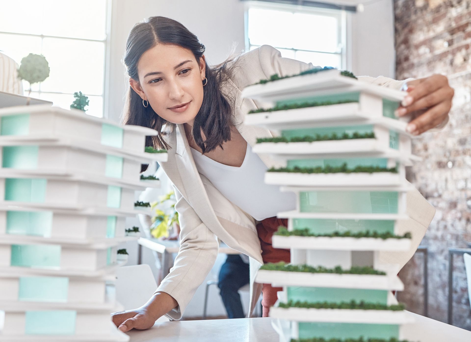 A woman is looking at a model of a building on a table contemplating leadership