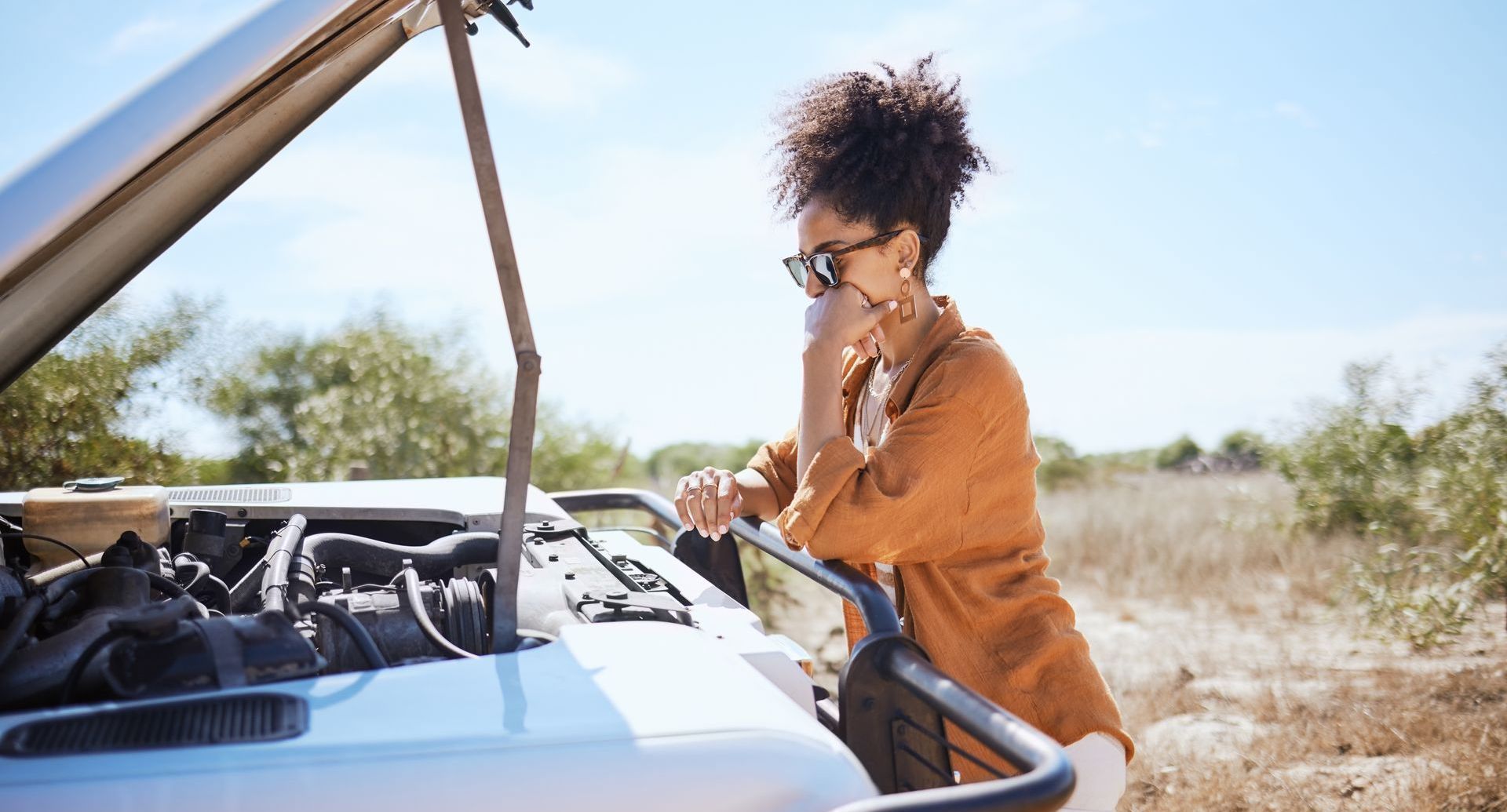 A woman examines her car's engine that's malfunctioning, contemplating the destination vs journey