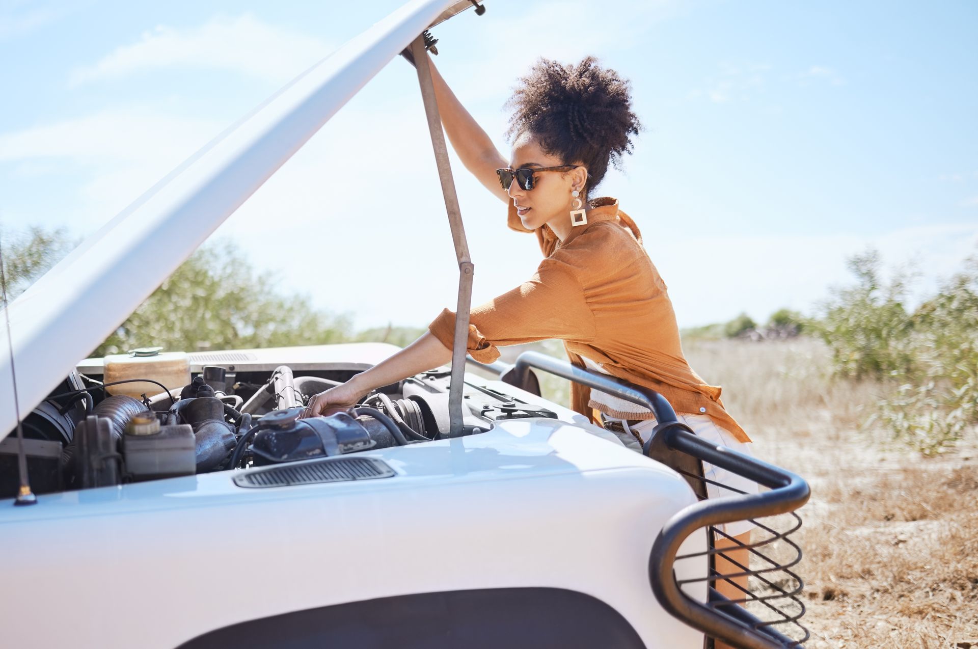 A woman examines her car's engine that's malfunctioning, contemplating the destination vs journey