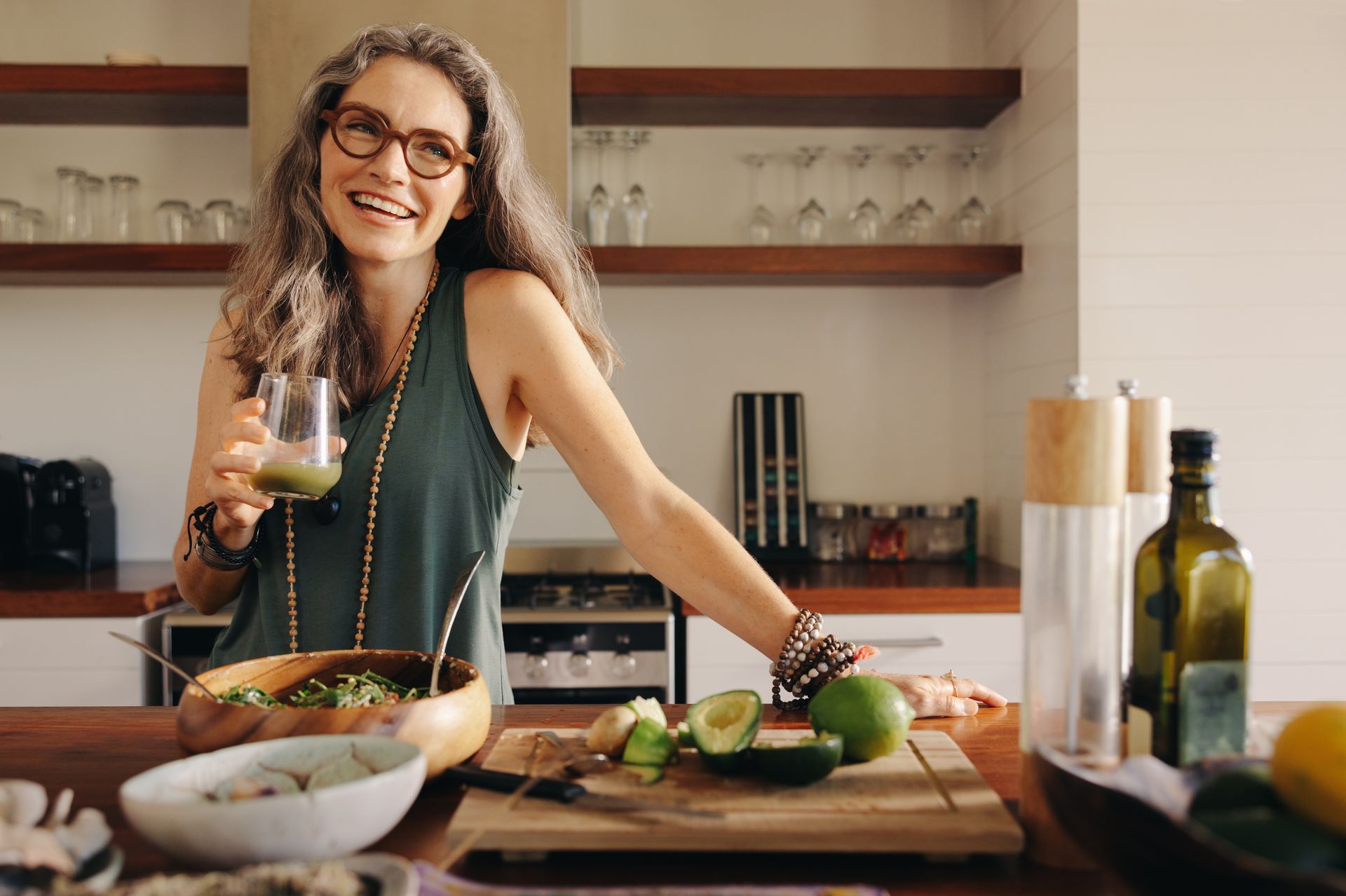 The same middle aged woman is in the kitchen preparing a salad, she is drinking a green juice, she knows the benefits of self awareness | benefits of being self aware