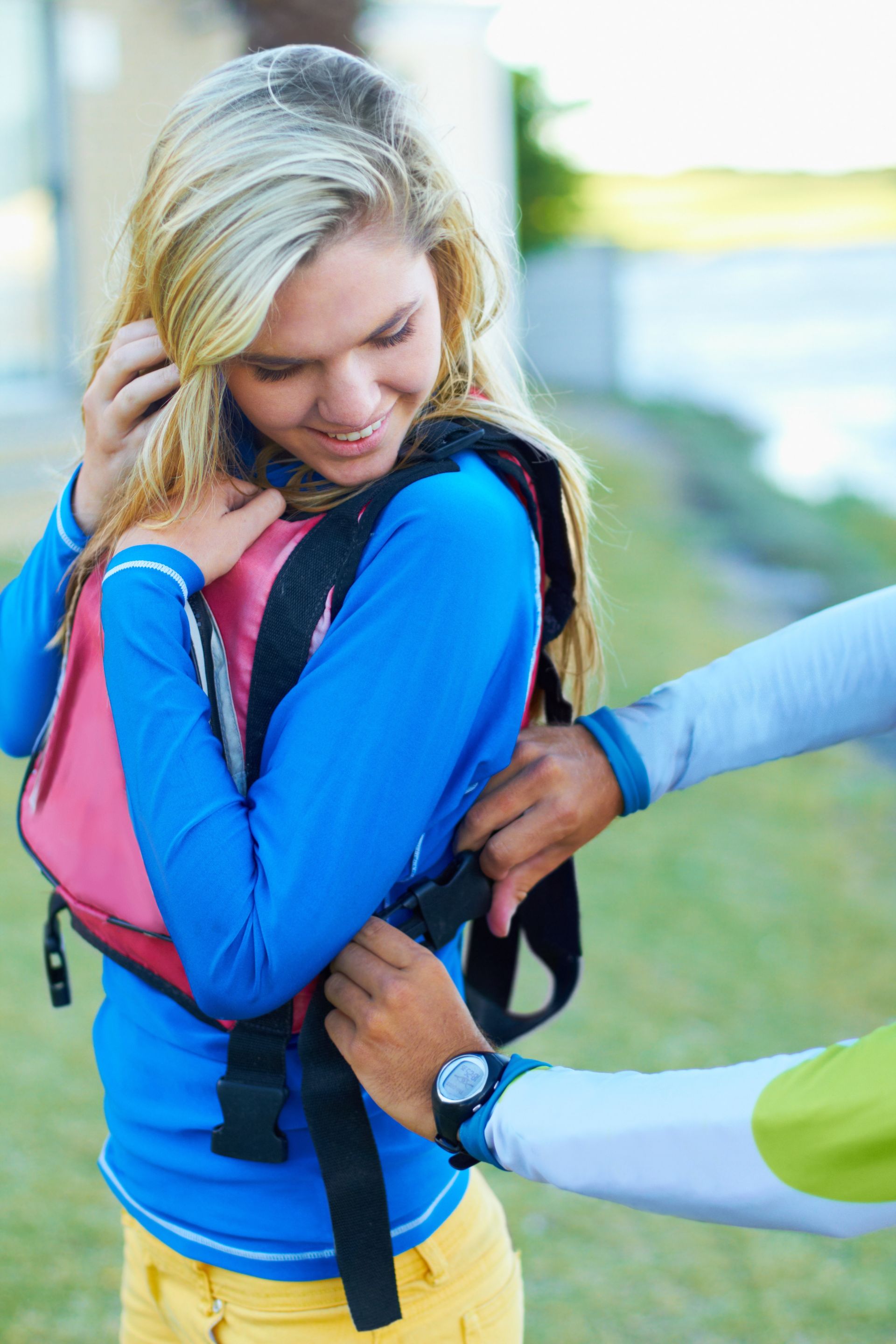 A young blonde woman is getting fitted for a life jacket, she is learning to kyak and in turn, turning weakness into strength