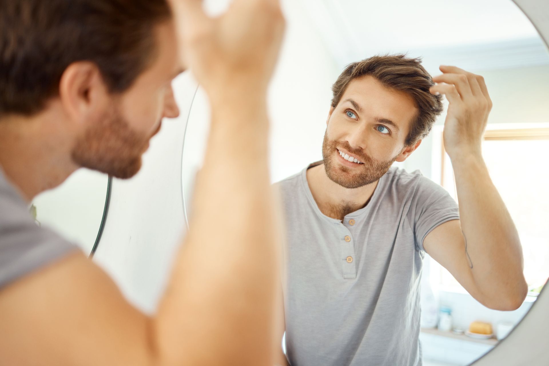 A man is looking at his hair in the mirror practicing gratitude and using positive affirmations because mindset is everything