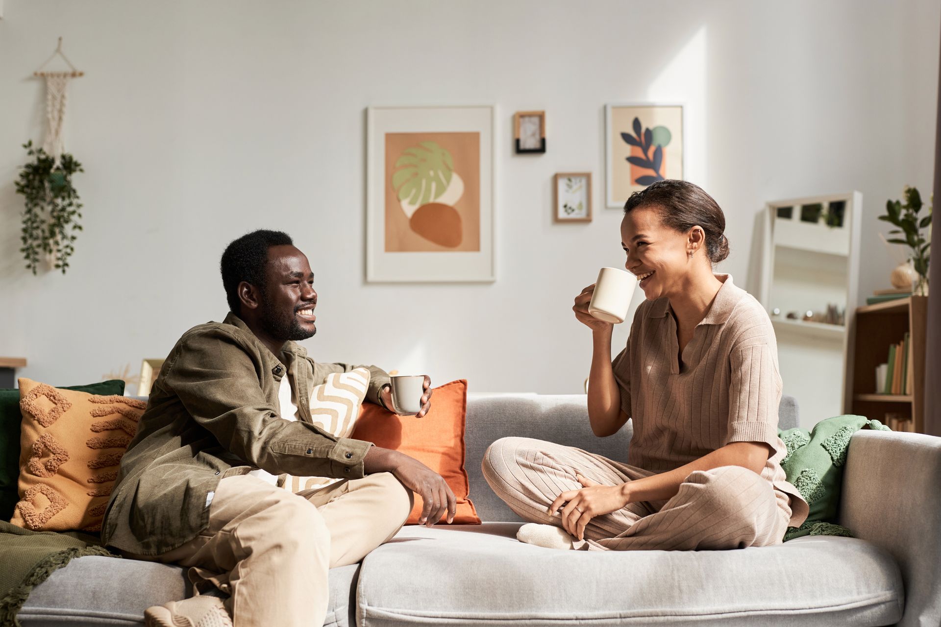 a man and a woman are sitting on a couch drinking coffee smiling, proving that mindset is everything