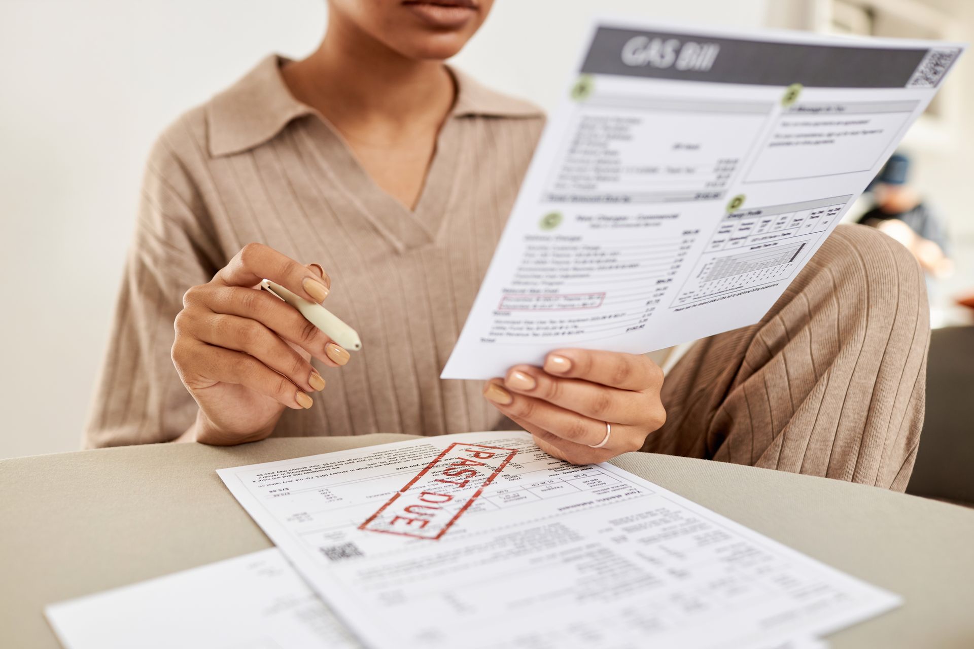 a woman is sitting at a table holding a past due bill and a pen, she is thinking about keeping a positive mindset