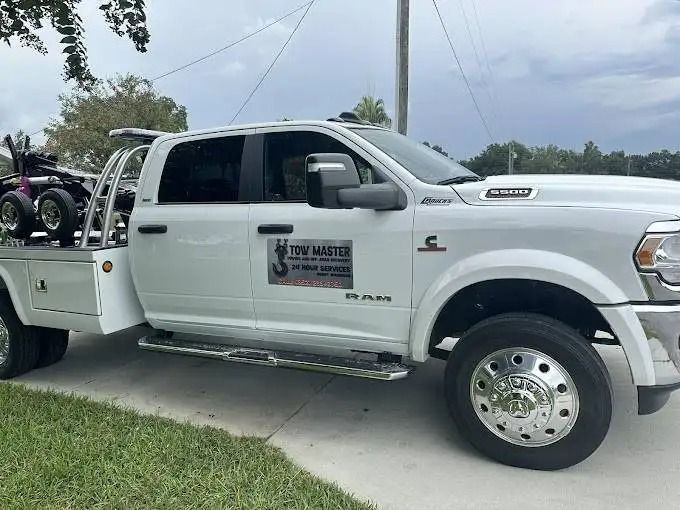 A white tow truck with a trailer attached to it is parked in a driveway.