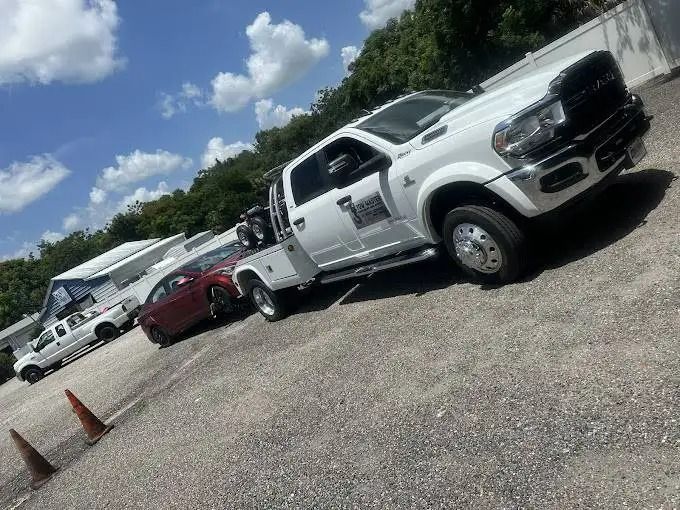 A white tow truck is parked in a parking lot next to a red car.