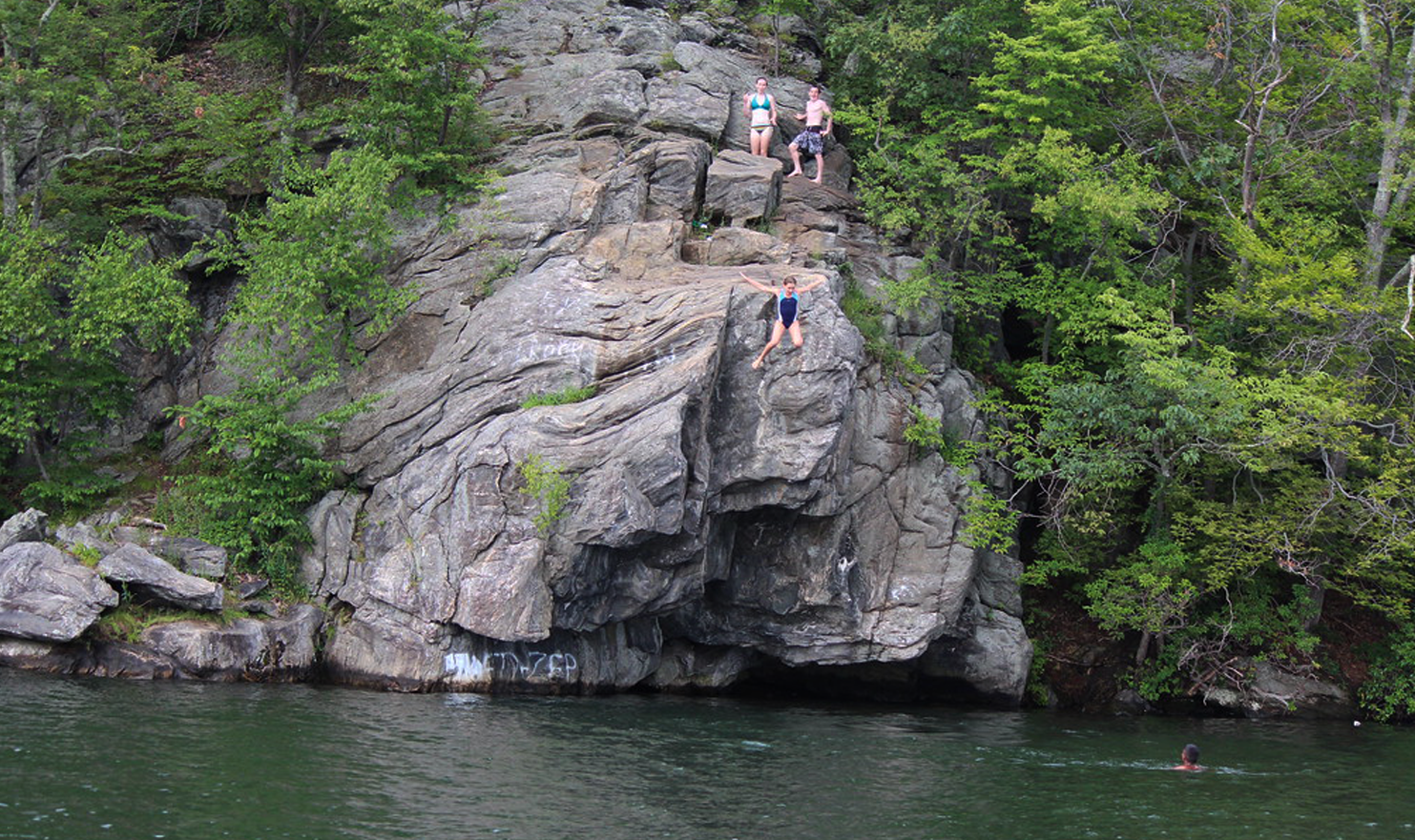 A group of people are jumping off a rock into a lake.