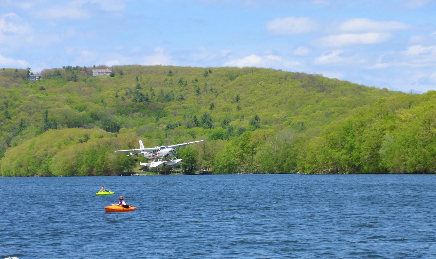 A man in a kayak is floating on a lake with a plane in the background.