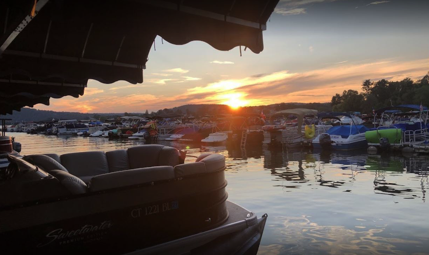 A pontoon boat is docked at a marina at sunset.