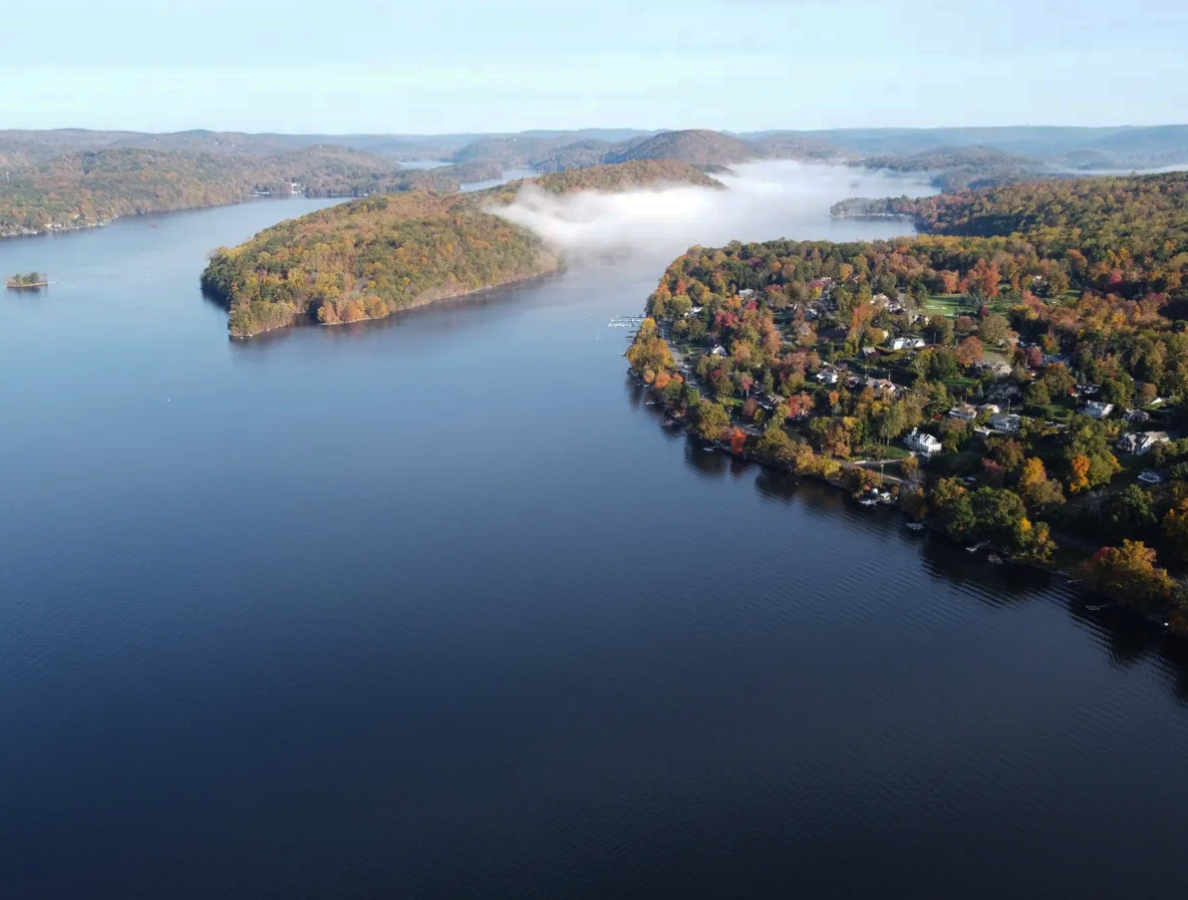 An aerial view of a lake surrounded by trees on a sunny day.