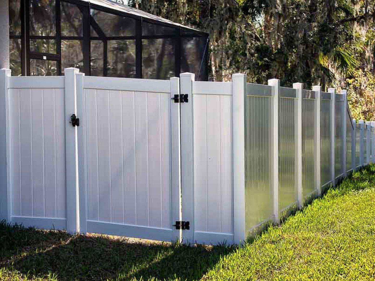 A white fence with a black gate is surrounded by green grass.