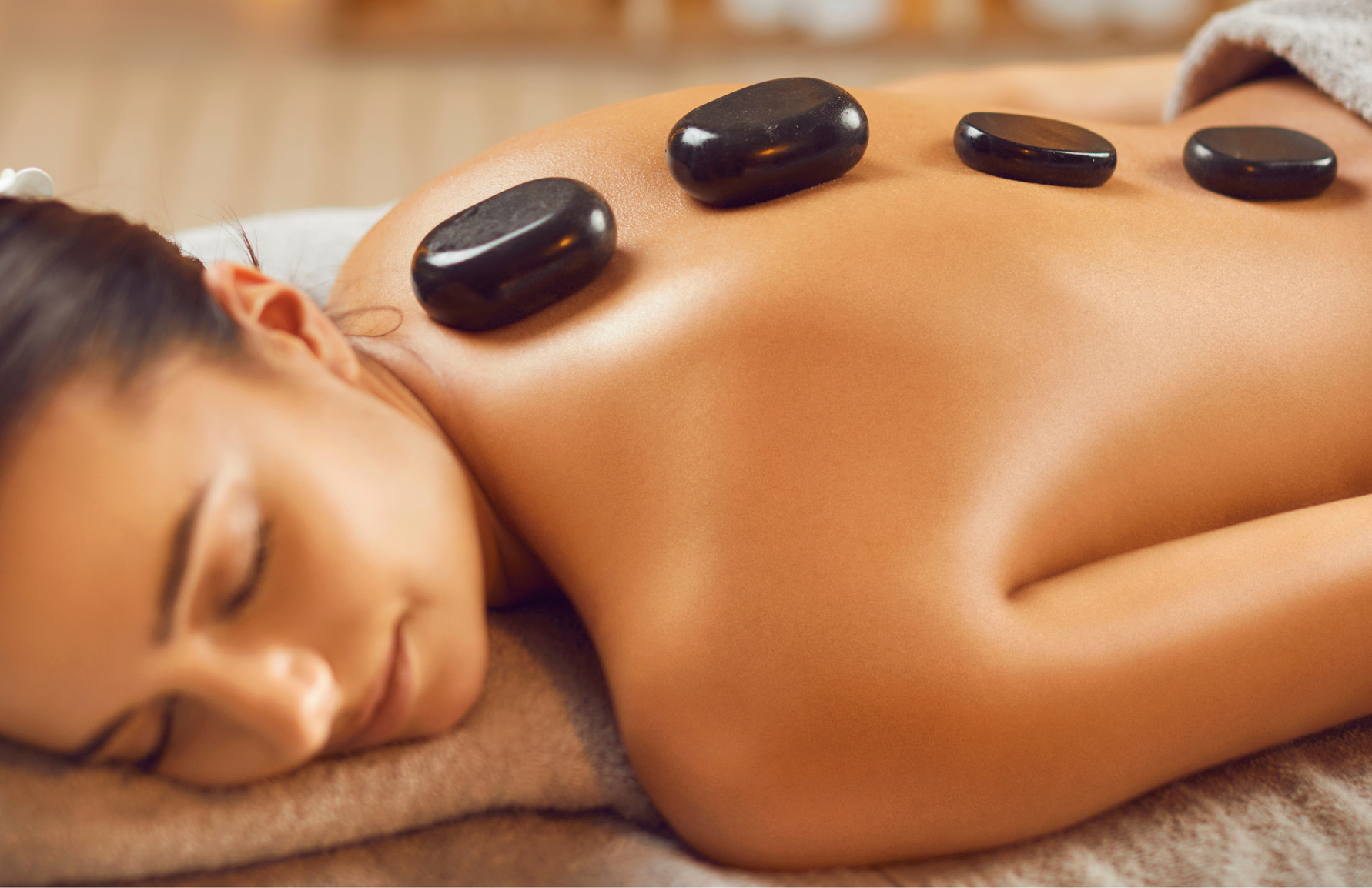 Woman receiving a hot stone massage, lying face down on a massage table, with black stones on her back.