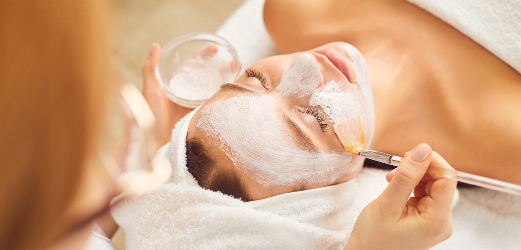 A person receiving a facial mask treatment at a spa, with a therapist applying the product.