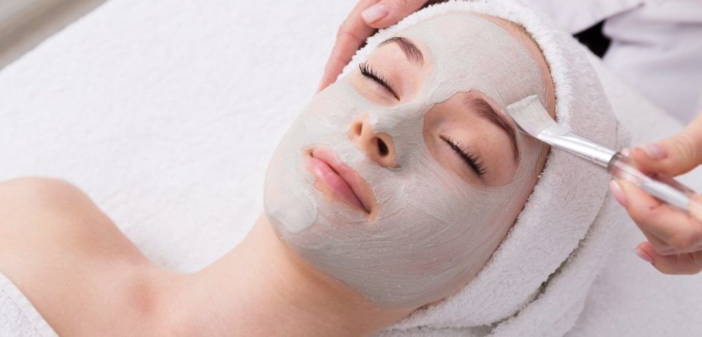 Woman has face mask treatment applied by technician with a small brush