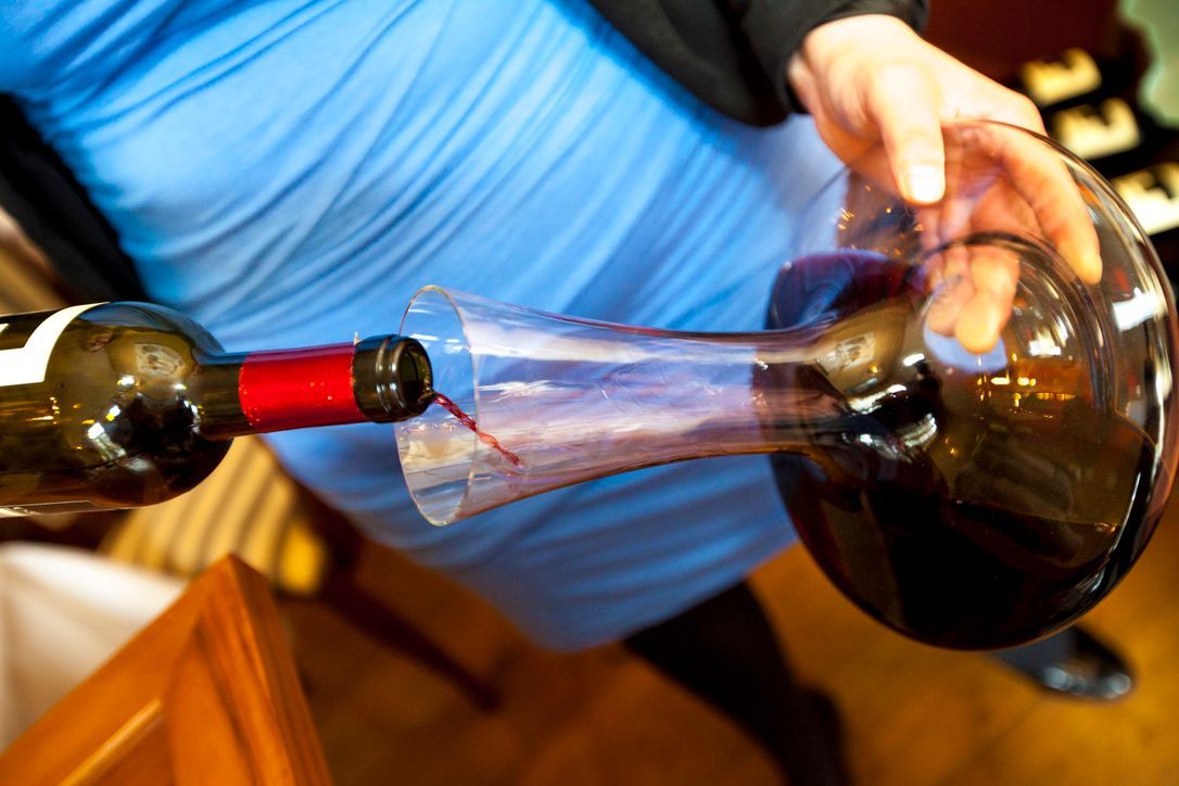 Persoon giet rode wijn uit een fles in een glazen karaf.