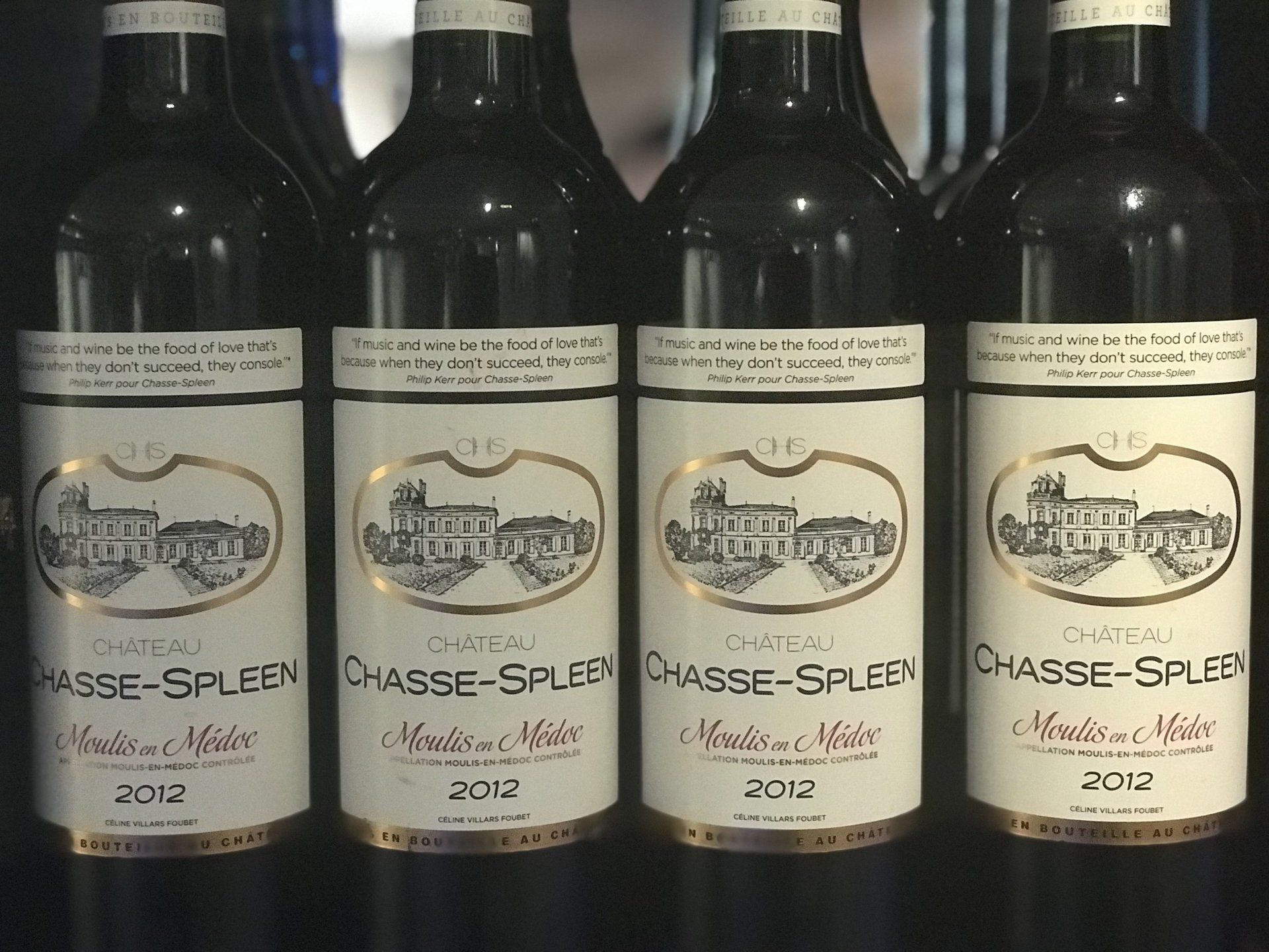 Vier flessen wijn van Château Chasse-Spleen, jaargang 2012, met witte etiketten en gouden accenten, in een donkere setting.