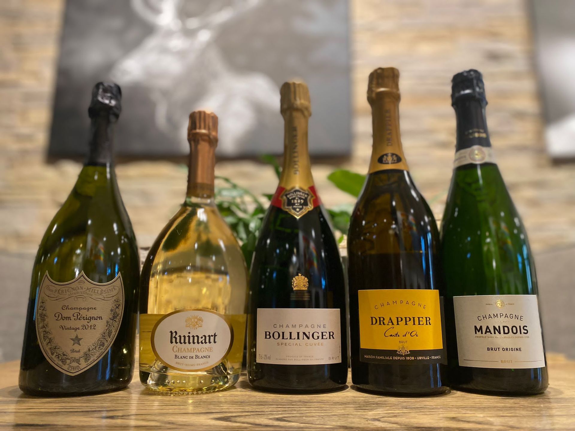 Vijf flessen champagne op een rij; verschillende merken met gouden en zwarte etiketten.