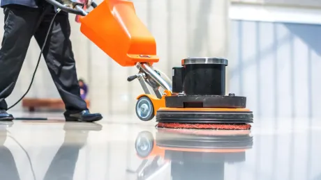 A person polishes a shiny floor with an orange and black floor buffer.