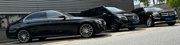 Drie zwarte Mercedes-Benz voertuigen staan ​​op een rij geparkeerd tegen een grijze muur.