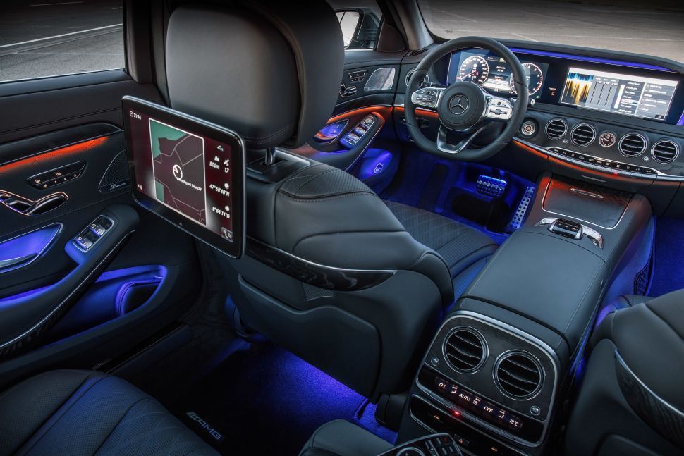 Interieurfoto van een luxe auto met zwarte lederen stoelen, infotainmentscherm achterin en sfeerverlichting in blauw.