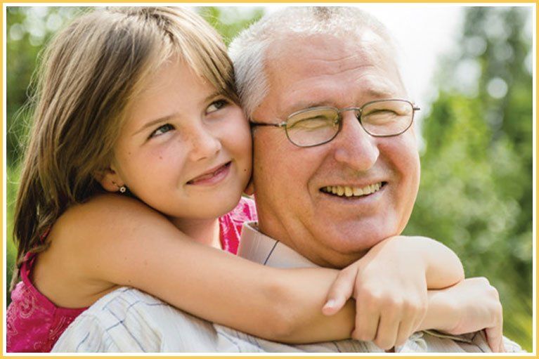 A little girl is hugging an older man who is wearing glasses.