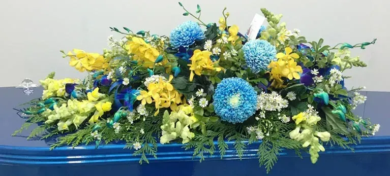 A blue coffin with yellow and blue flowers on it.