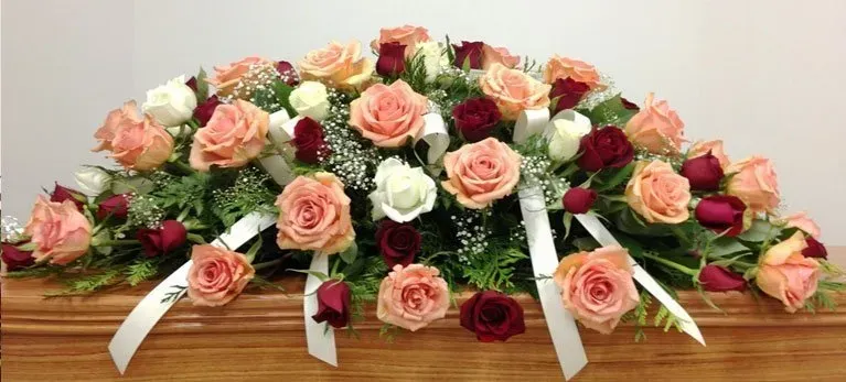 A casket is decorated with roses and ribbons for a funeral.