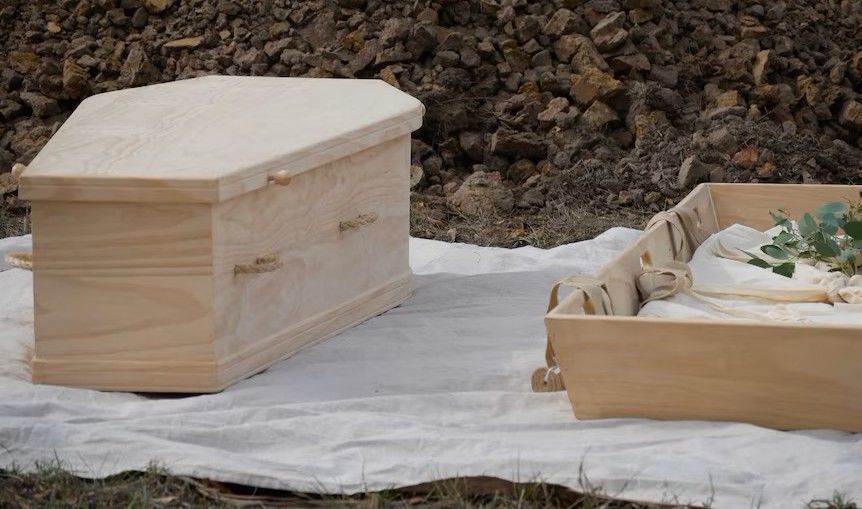 A wooden coffin is sitting on top of a white blanket.