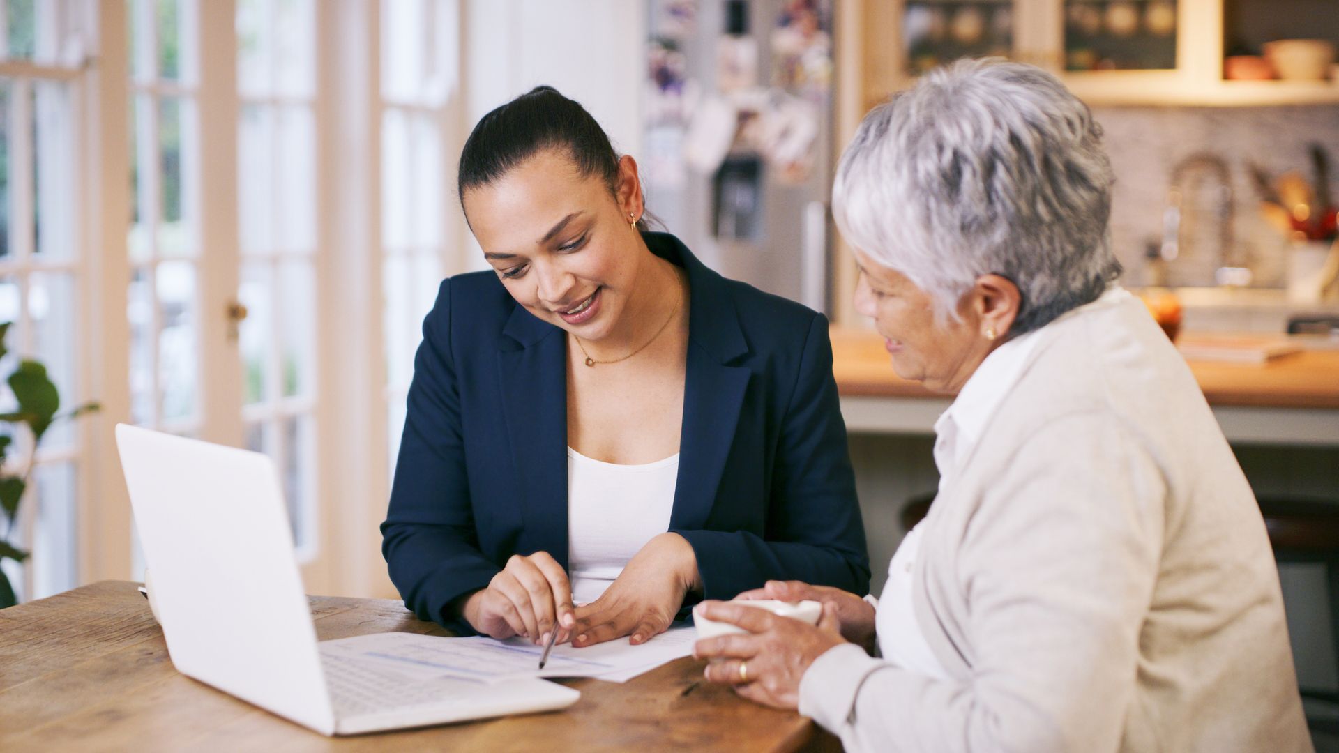 Two women are sitting at a table looking at a laptop.