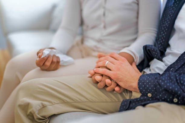 A man and a woman are holding hands while sitting on a couch.