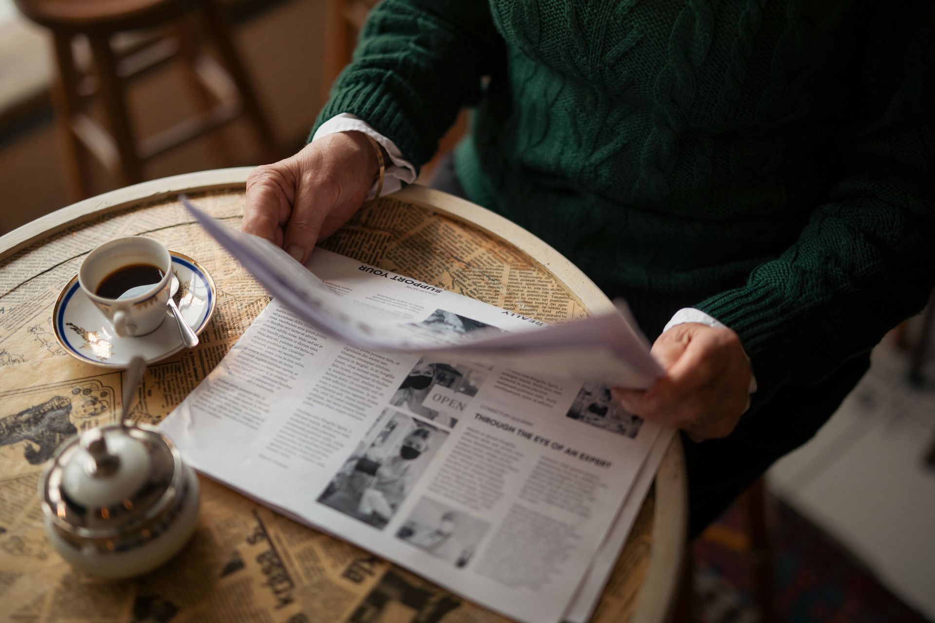 A man is sitting at a table reading a newspaper.