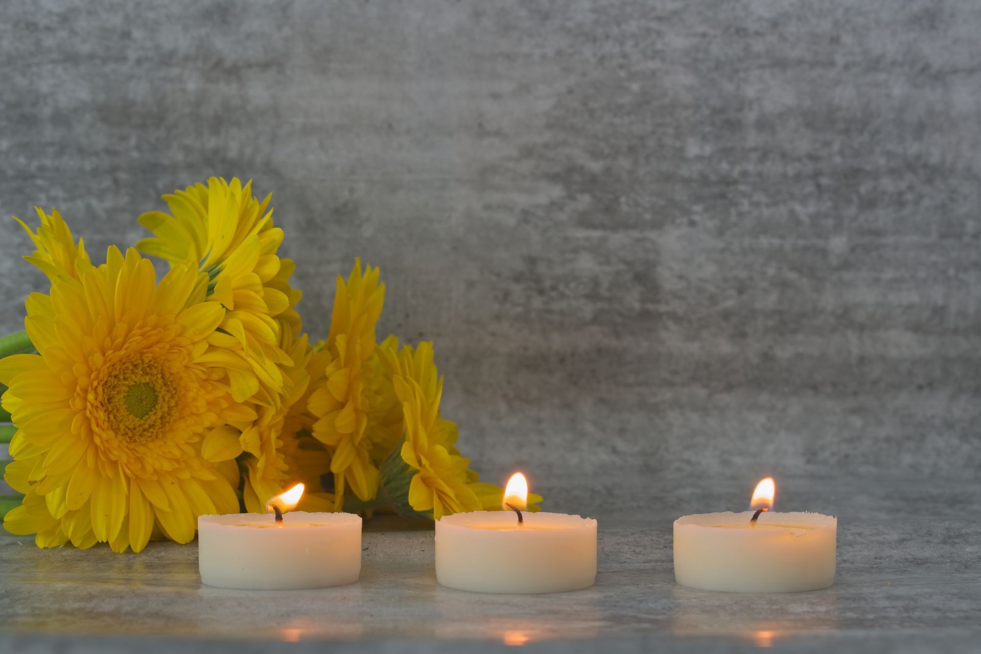 Three lit candles and yellow flowers on a table.