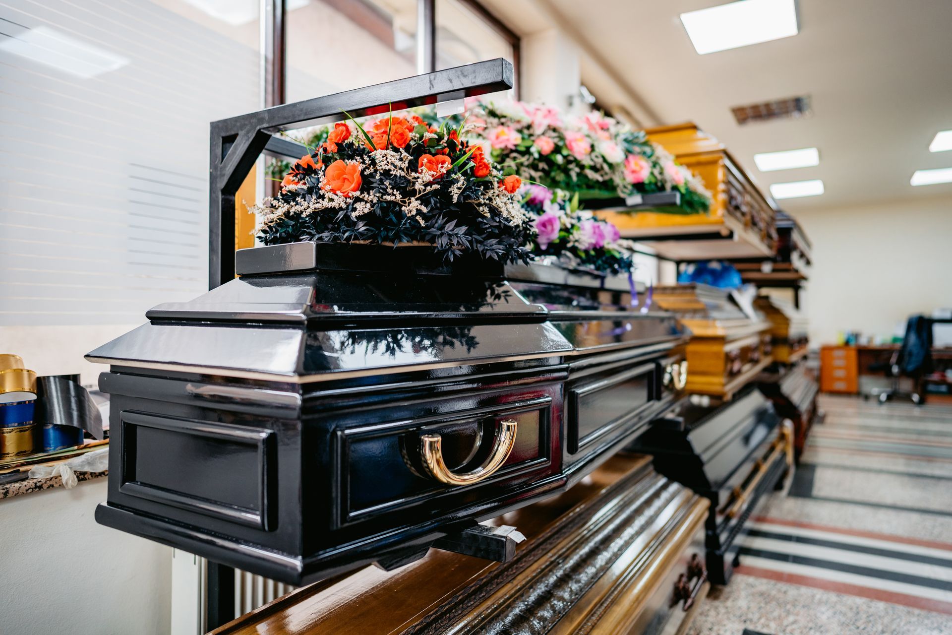 A black coffin with flowers on top of it is on display in a funeral home.