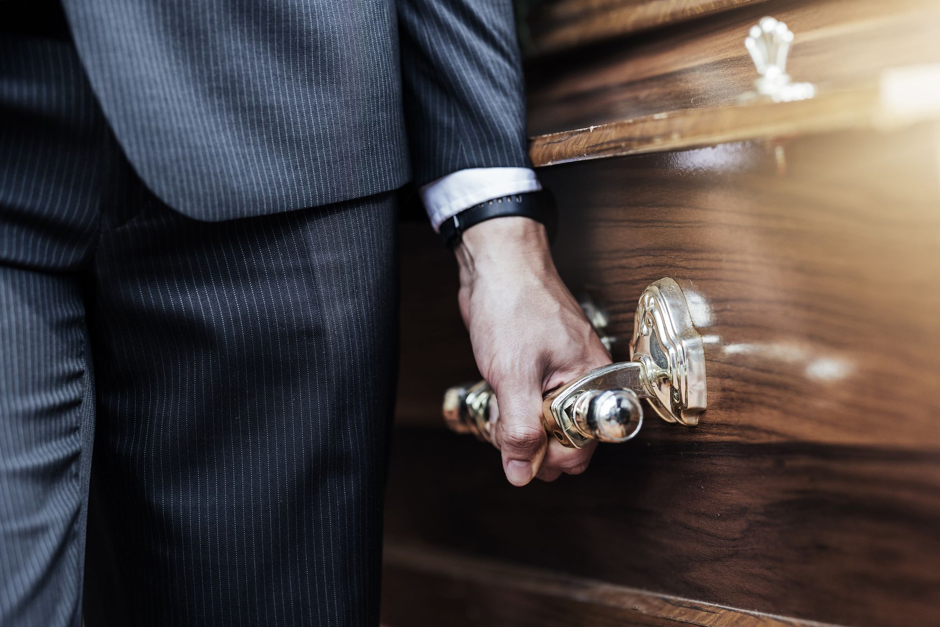 A man in a suit is holding the handle of a wooden coffin.