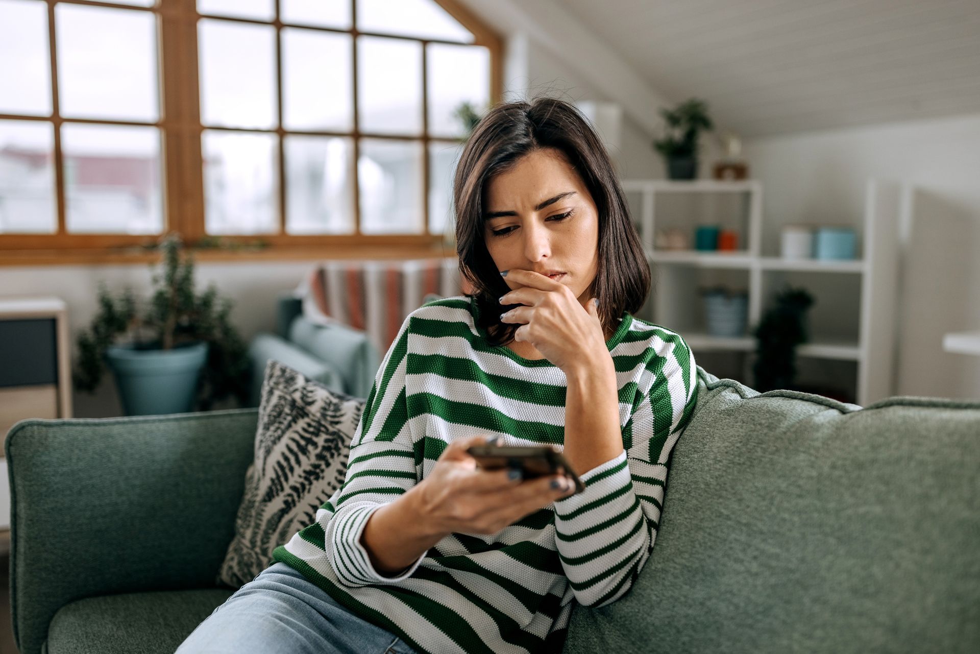 A woman is sitting on a couch looking at her cell phone.