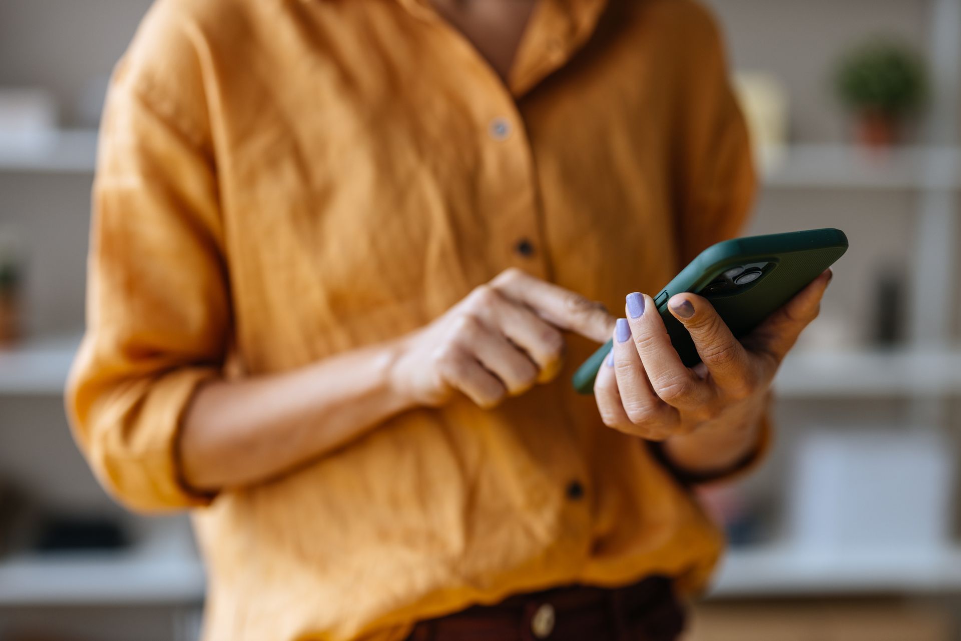 A woman in a yellow shirt is using a smart phone.