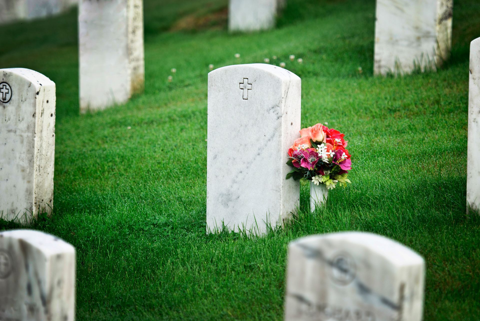 A cemetery with lots of graves and flowers in the grass.