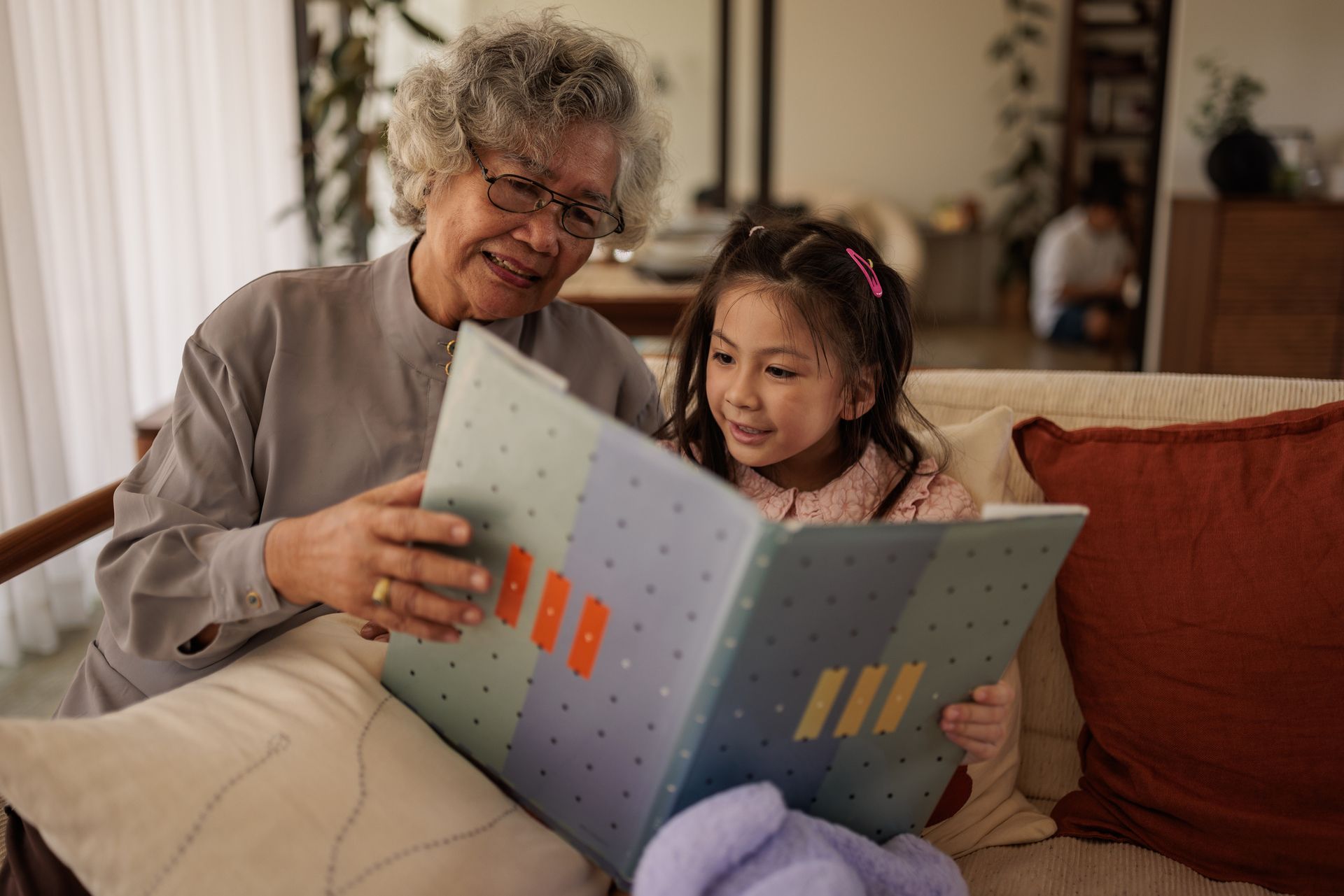 An elderly woman is reading a book to a little girl.