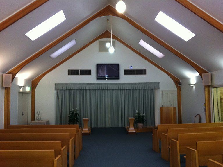 A church with rows of wooden benches and a television on the ceiling