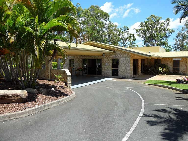 A large house with a curved driveway leading to it surrounded by palm trees.