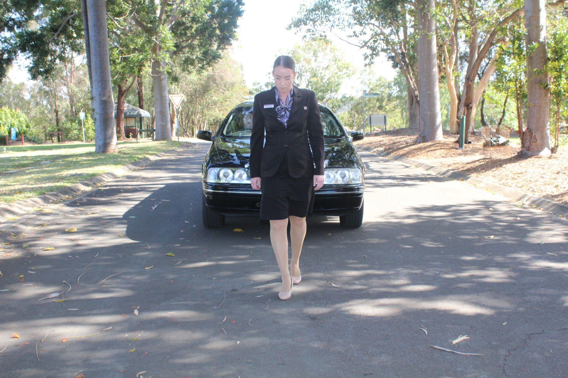 A woman in a suit is walking in front of a black car